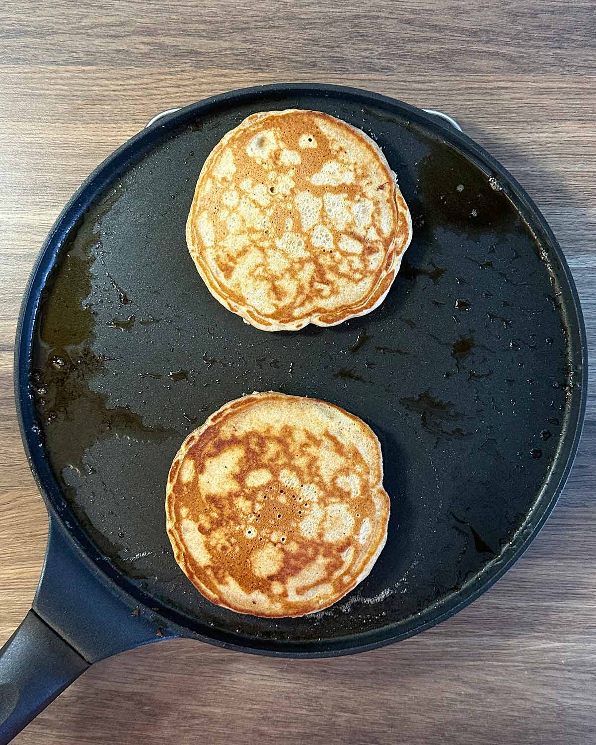 Two cooked pancakes in a frying pan.