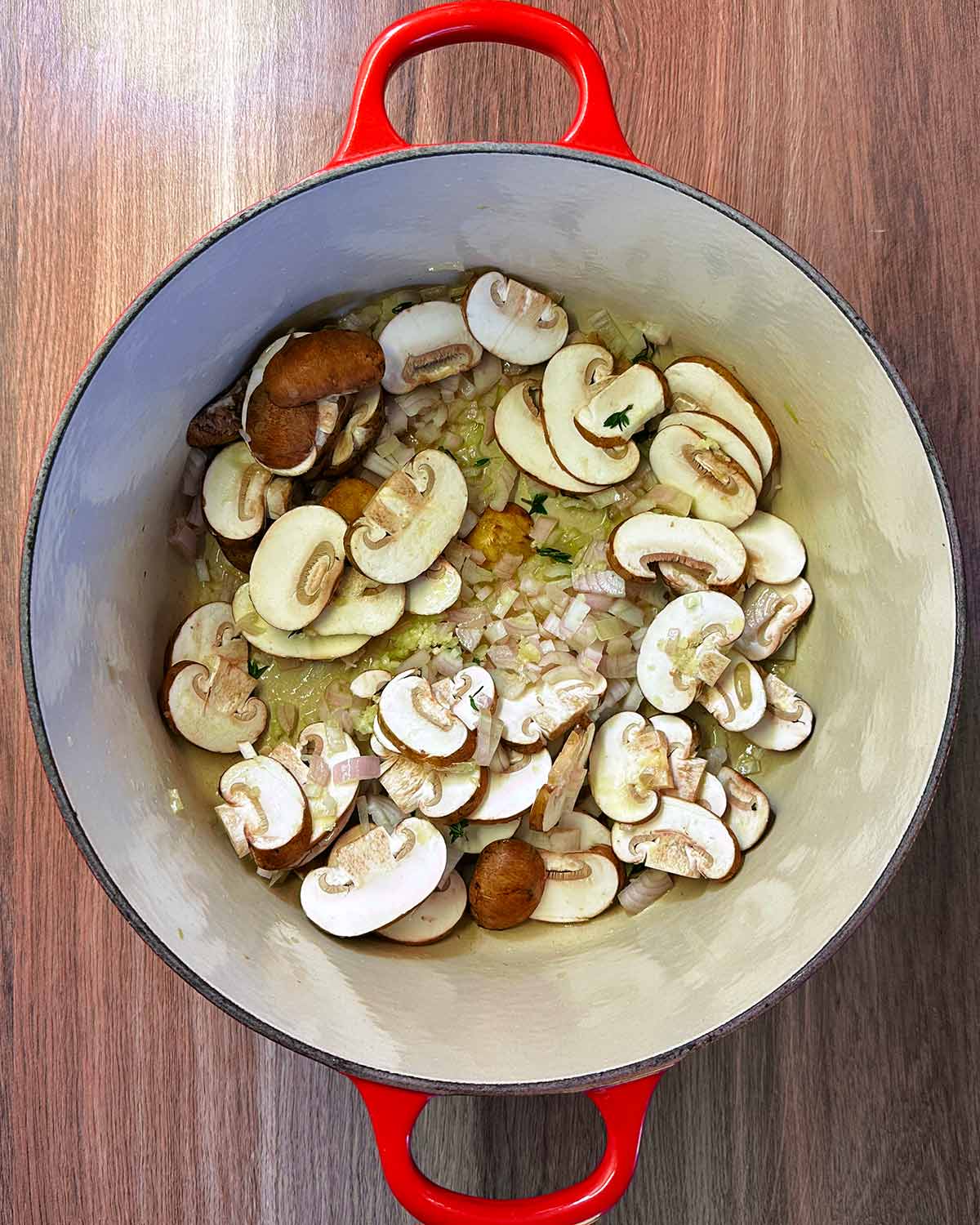 Chopped onions and sliced mushrooms cooking in butter in a large red pan.