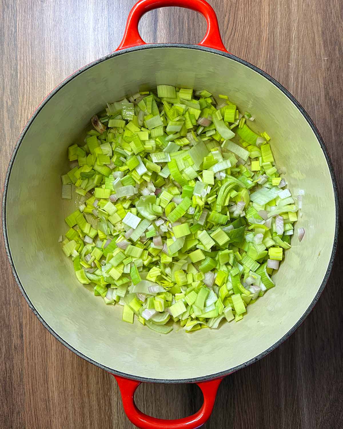 A large pan with chopped leeks and onions cooking in it.