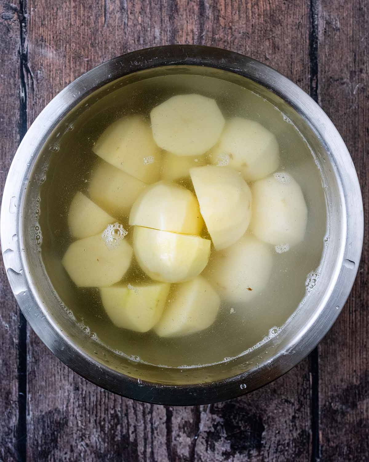 Pelled and halved potatoes in a bowl of water.