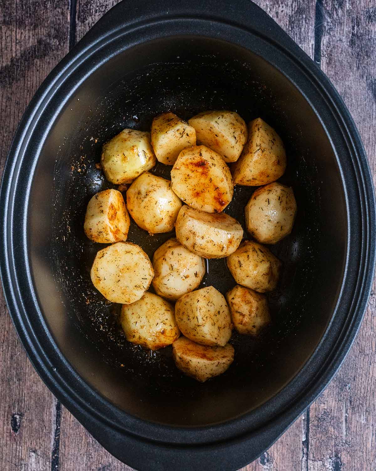 Uncooked potatoes, oil and seasoning in a slow cooker bowl.