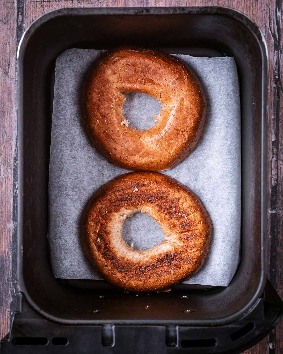 Two bagel halves in a paper lined air fryer.