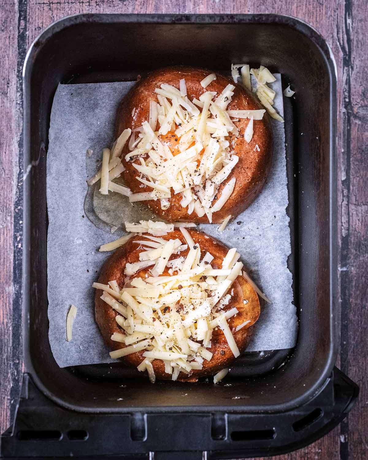 Eggs cracked into the bagel holes and grated cheese sprinkled over them.