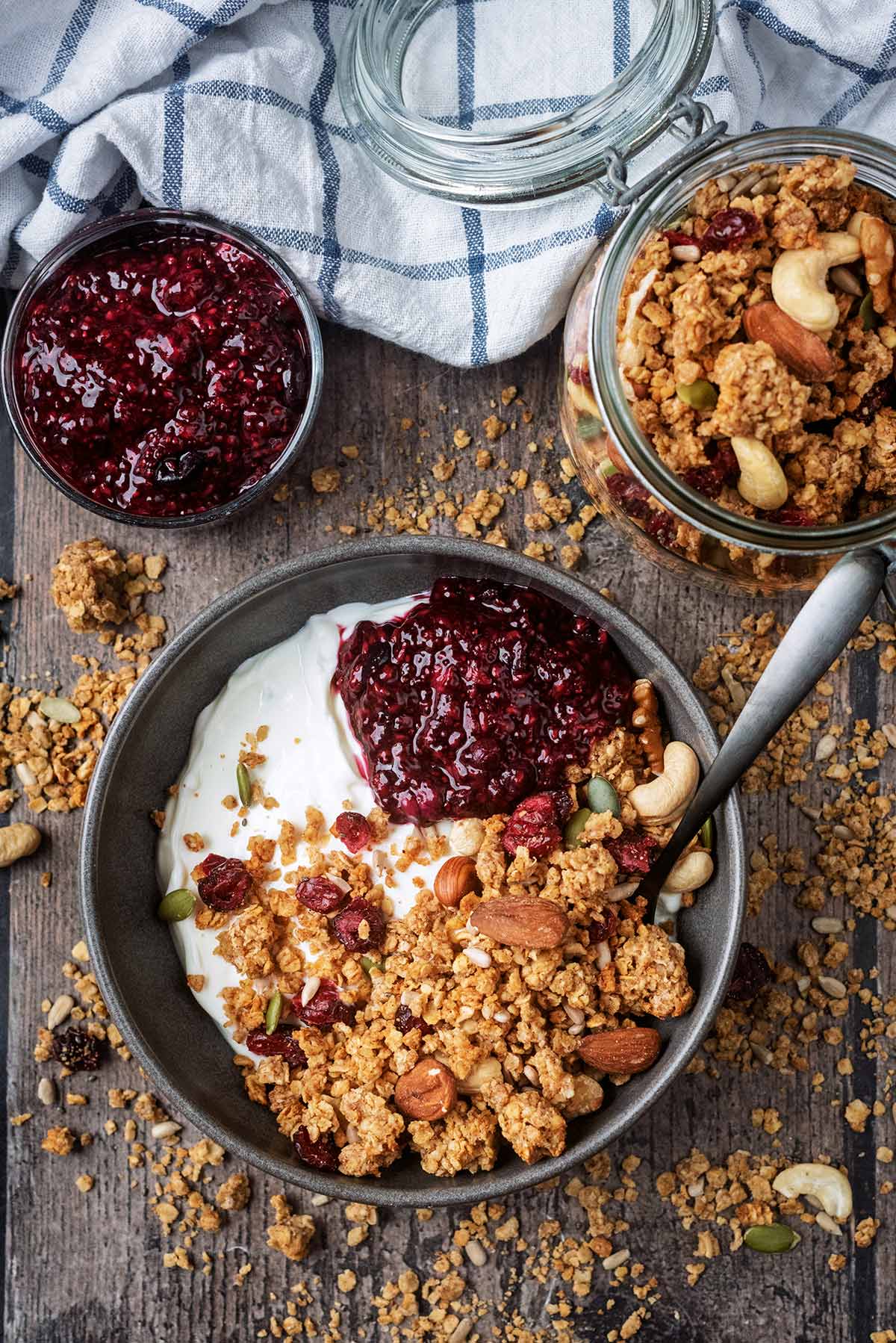 A bowl of granola topped yogurt next to a bowl of fruit compote and a jar of granola.