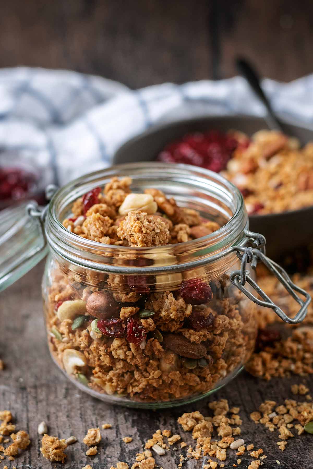 A glass jar full of granola in front of a bowl of granola topped yogurt.