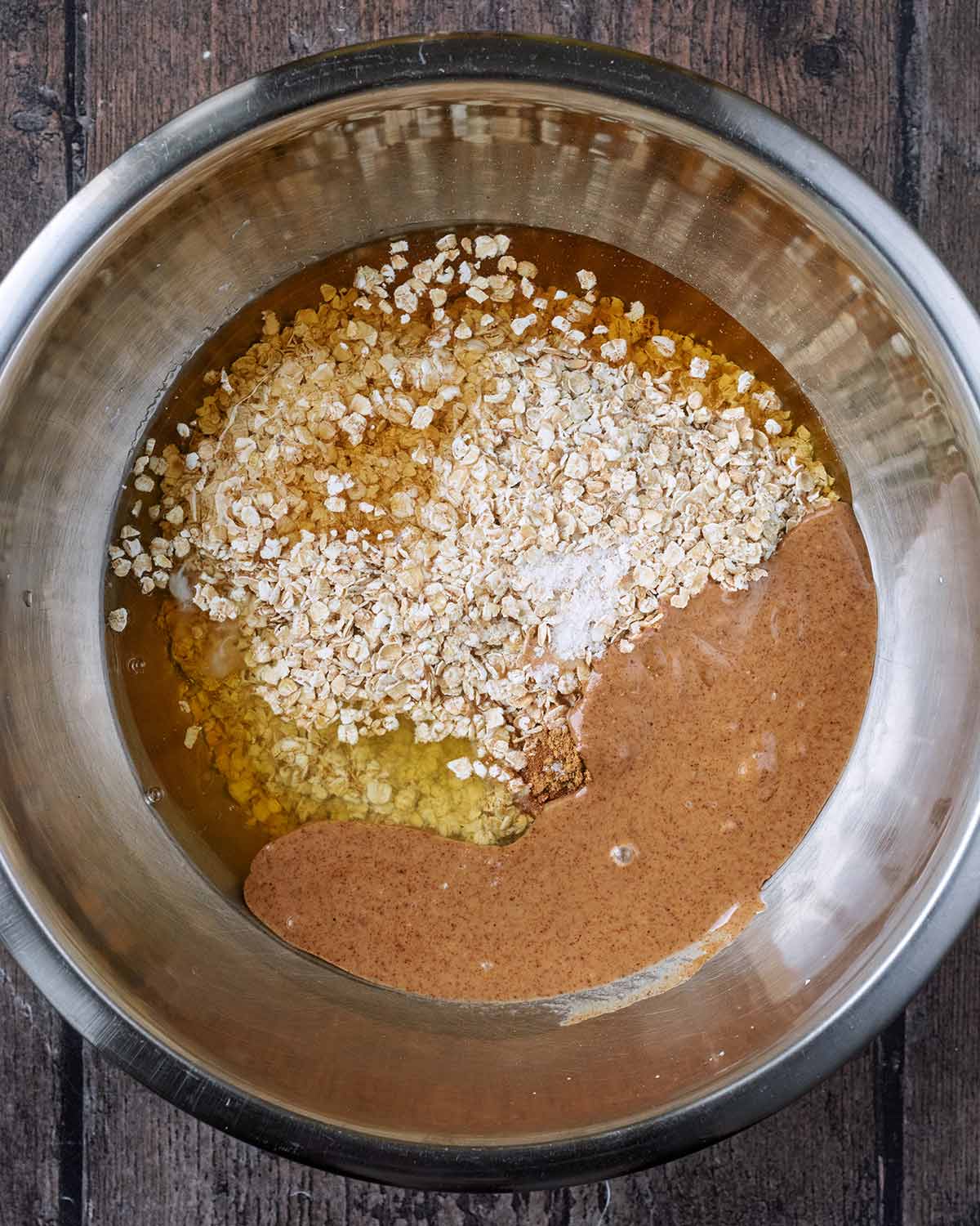 A mixing bowl containing oats, maple syrup, almond butter, egg white and spices.