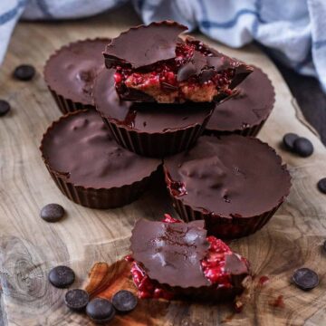 A pile of chocolate raspberry peanut butter cups on a wooden board.