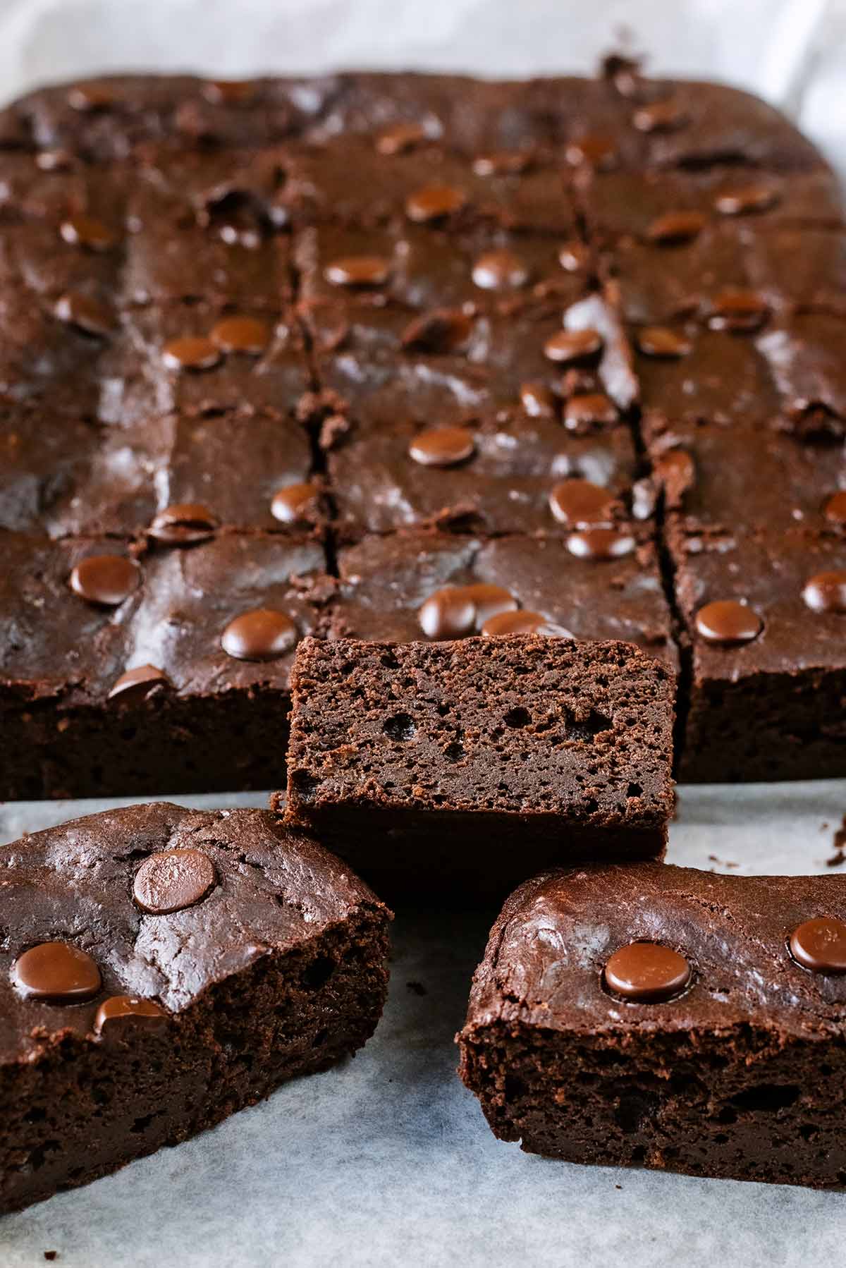 A slab of brownie cut into squares with three brownies in a pile at the front.