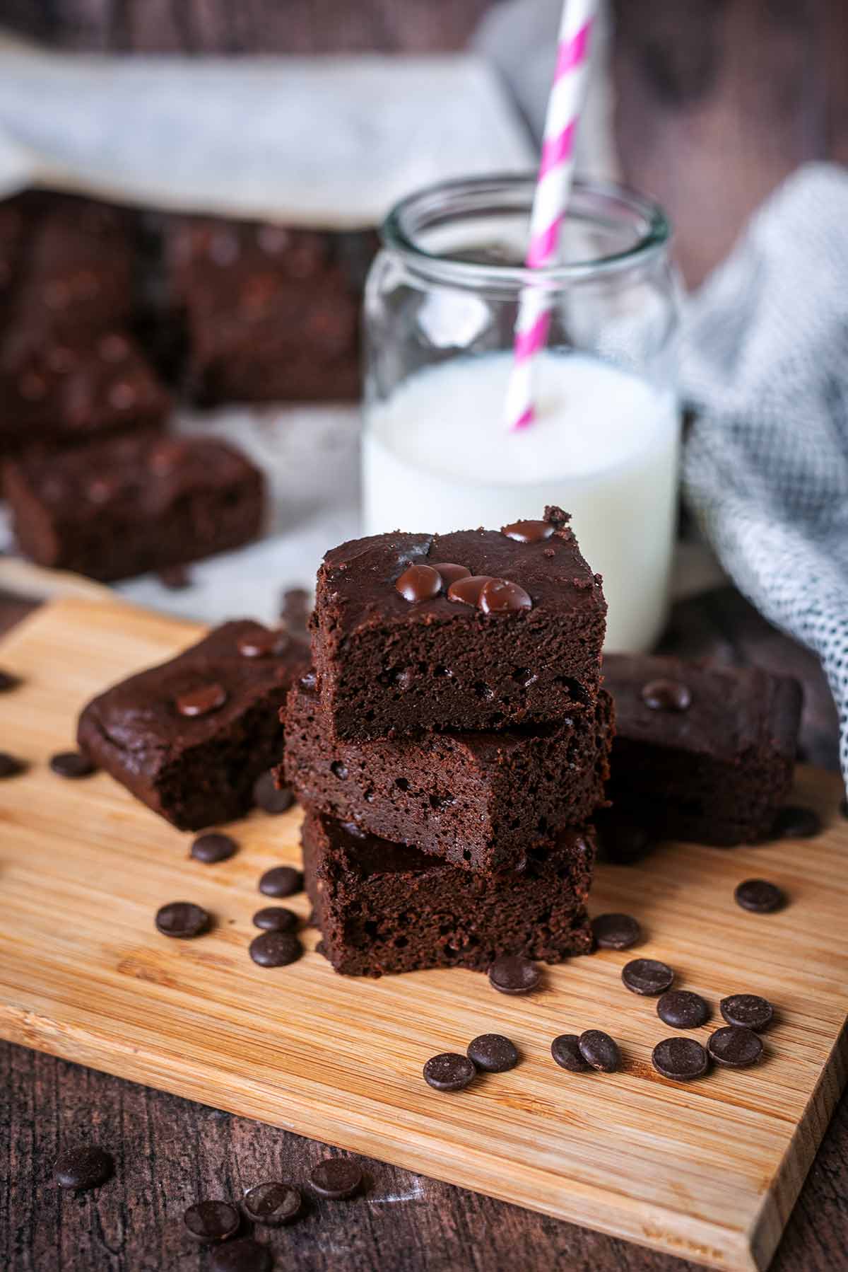 A stack of chocolate brownies on a wooden board with a glass of milk.