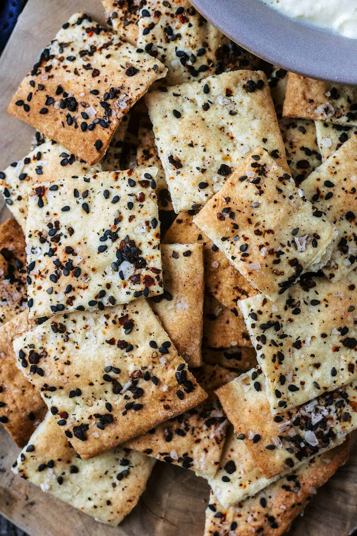 A pile of small square crackers seasoned with salt and black sesame seeds.