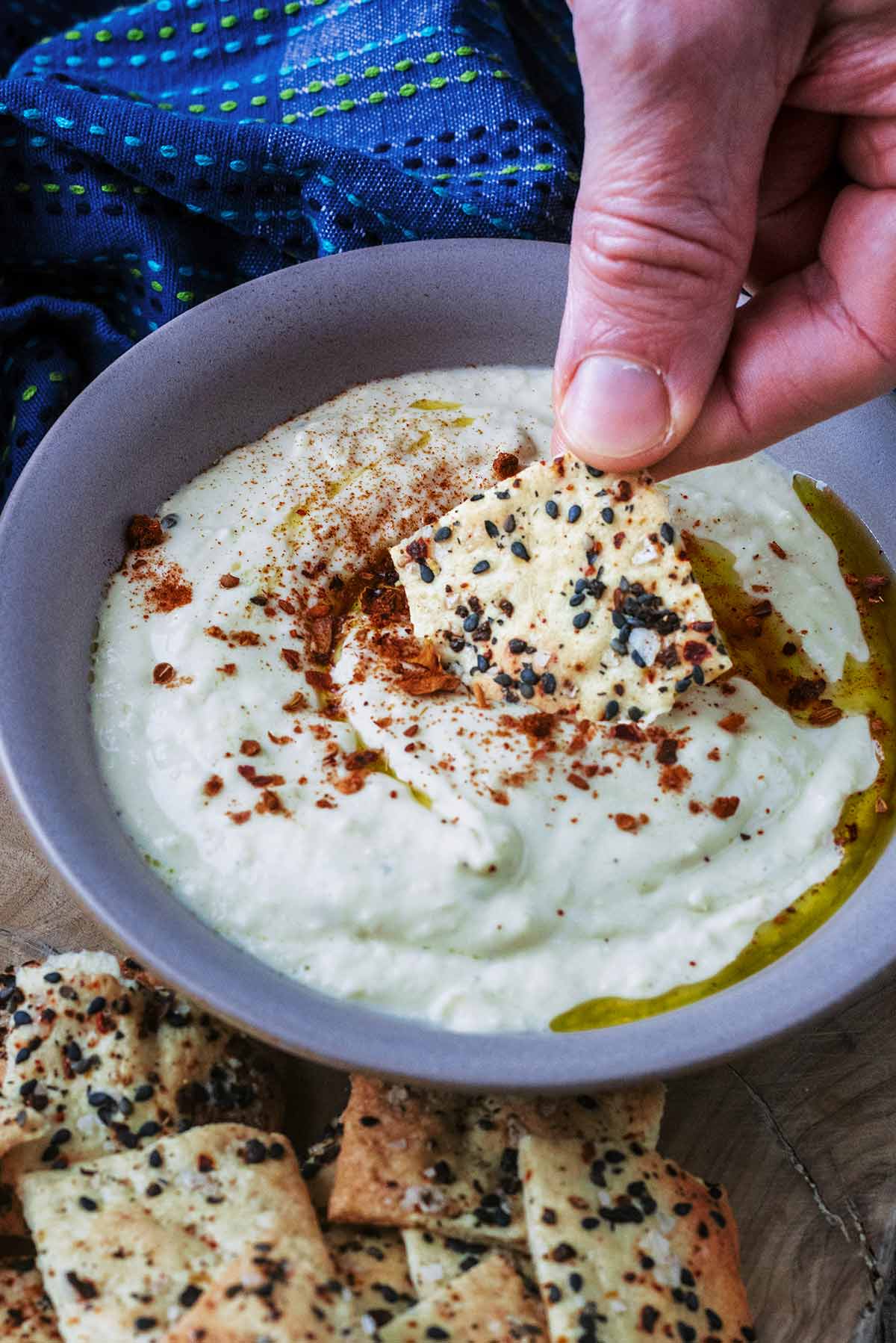 A small homemade cracker being dipped into some hummus.