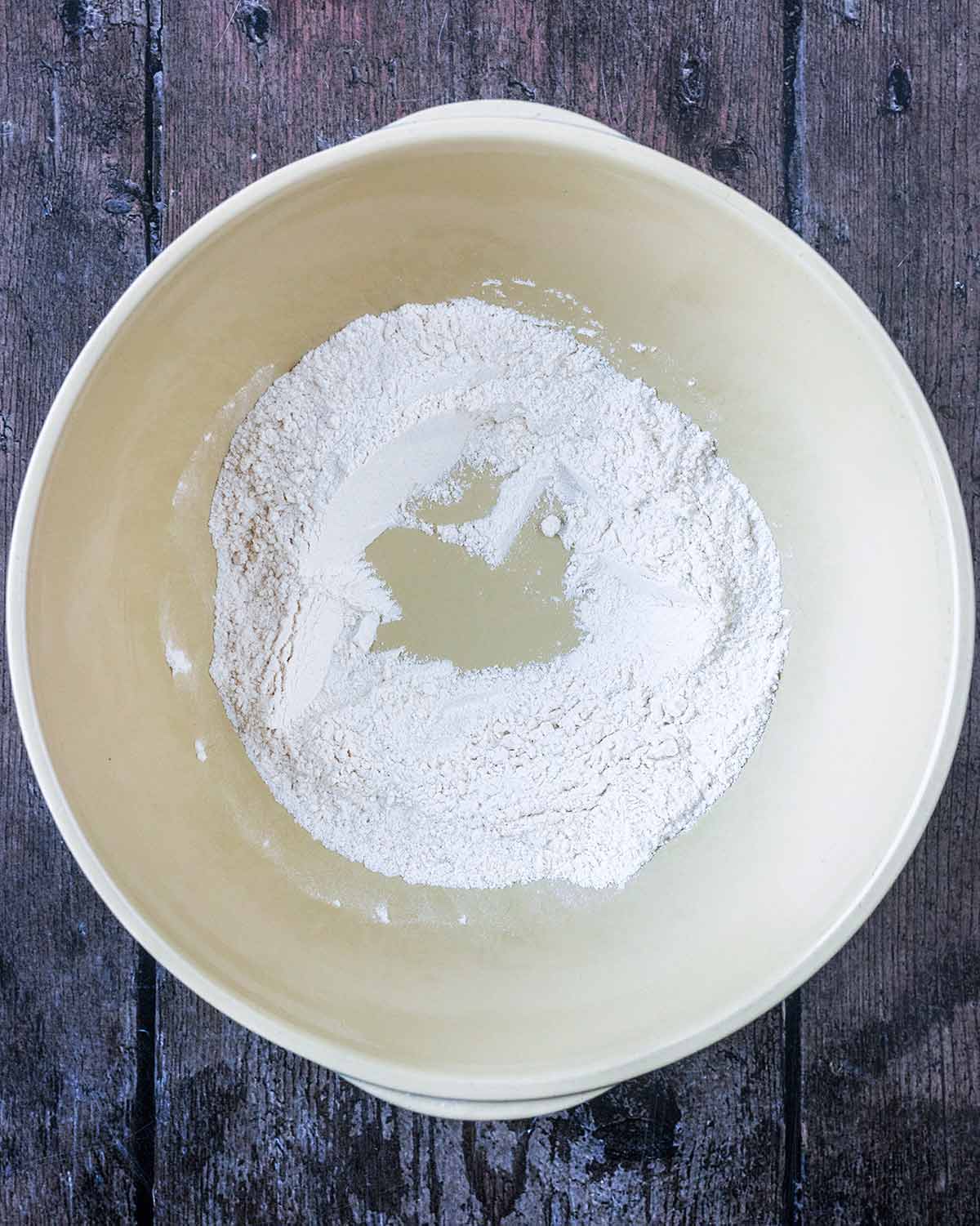 A mixing bowl containing flour. A well has been made in the flour.