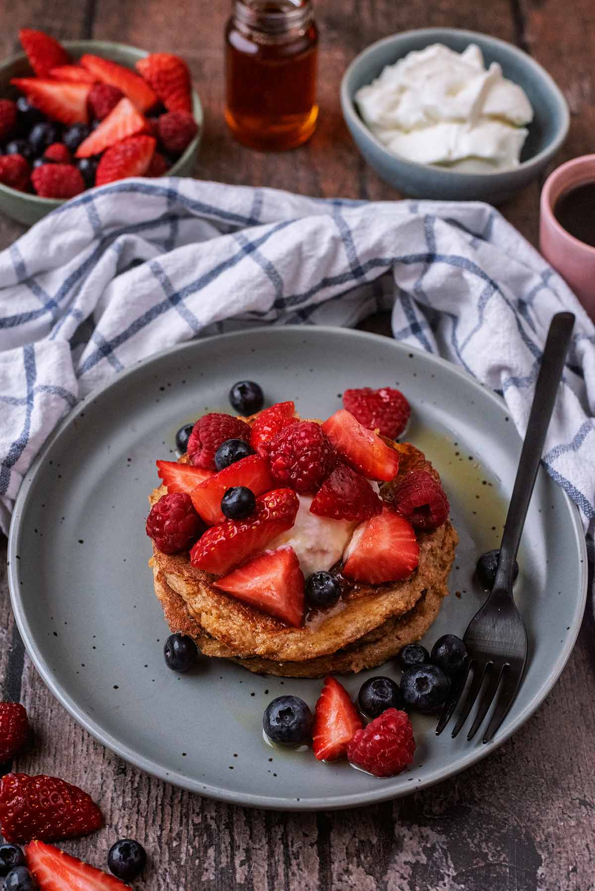 A stack of pancakes topped with berries and maple syrup.