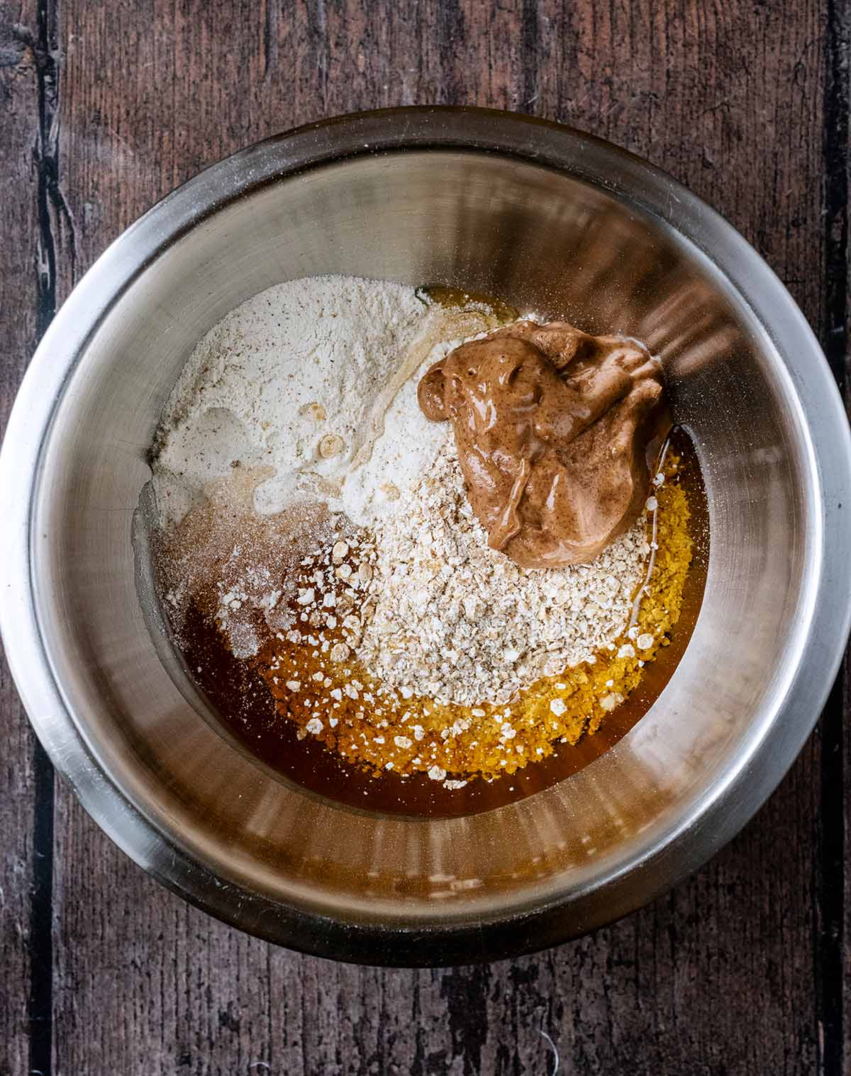 A mixing bowl containing oats, protein powder, vanilla, maple syrup and almond butter in it.