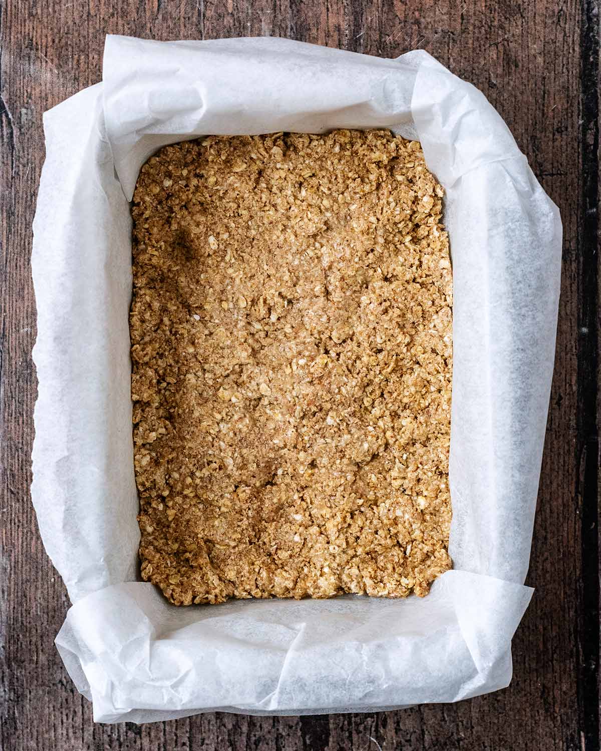 A lined baking tin with the oat mixture packed into the bottom.