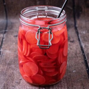 A jar of quick pickled radishes on a wooden surface.