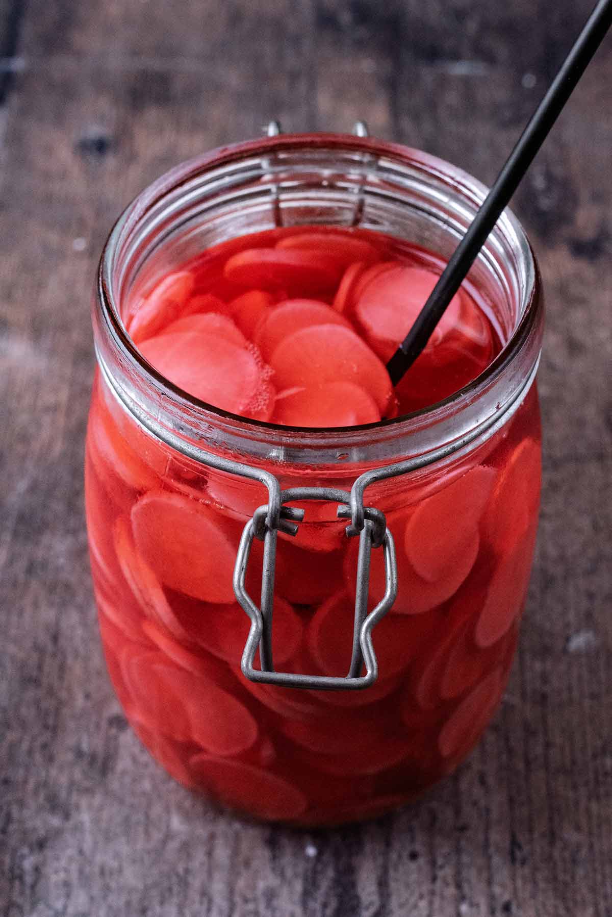 A jar of pickled radish slices with a fork in it.