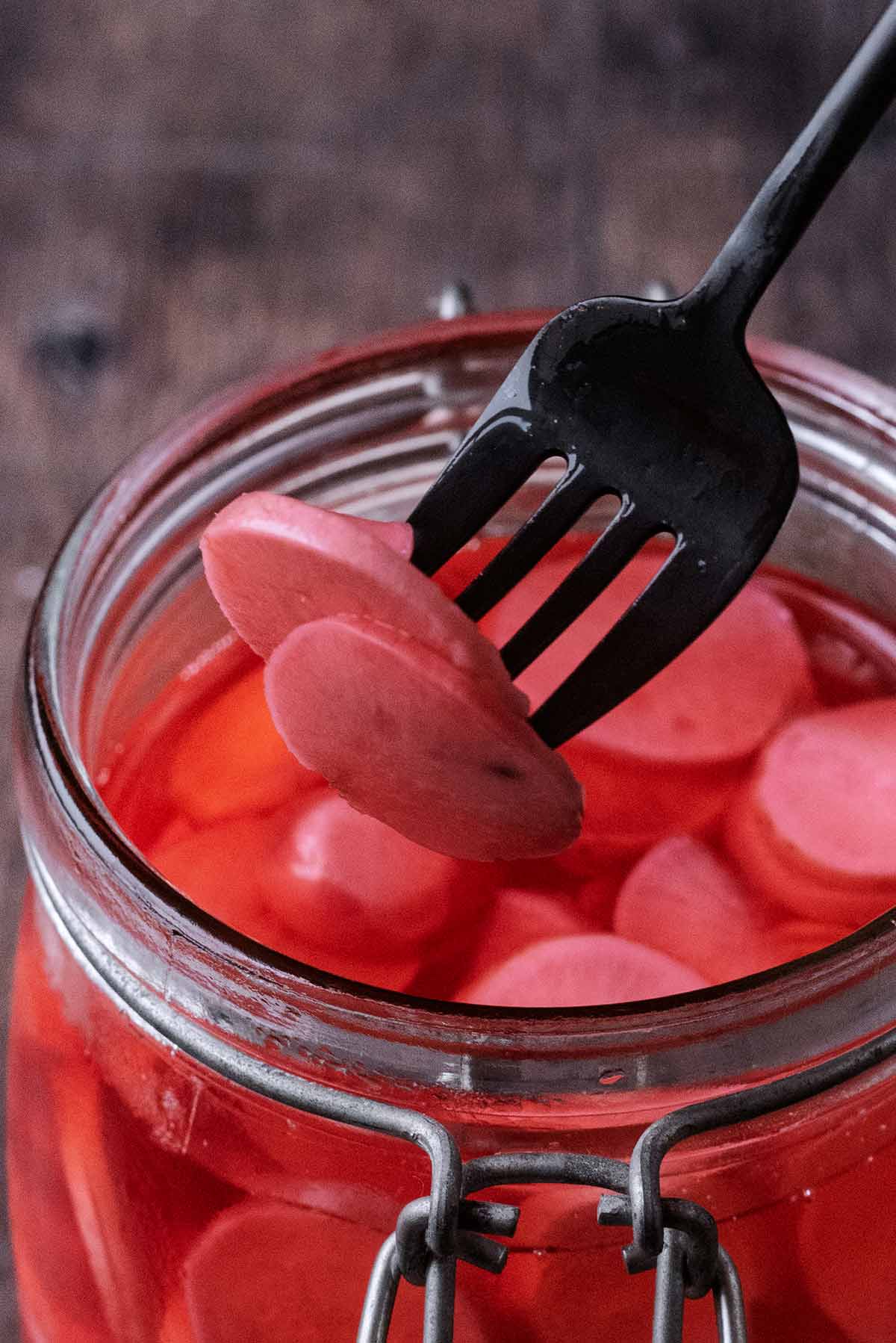 A fork lifting some pickled radishes out of a jar.