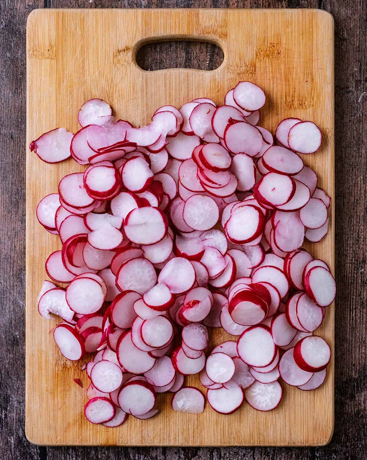 A wooden chopping board with sliced radishes on it.