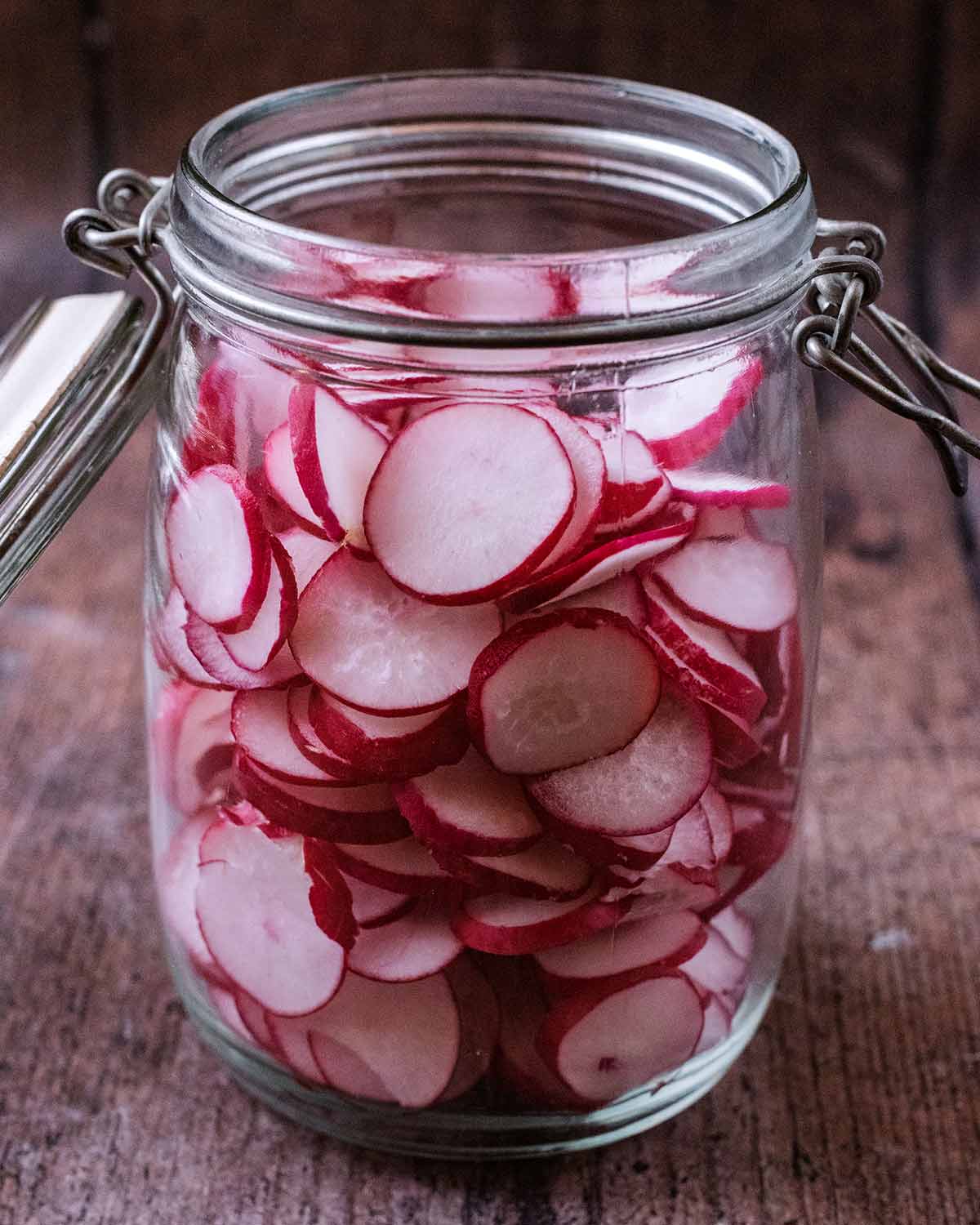 A large glass jar with sliced radishes in it.