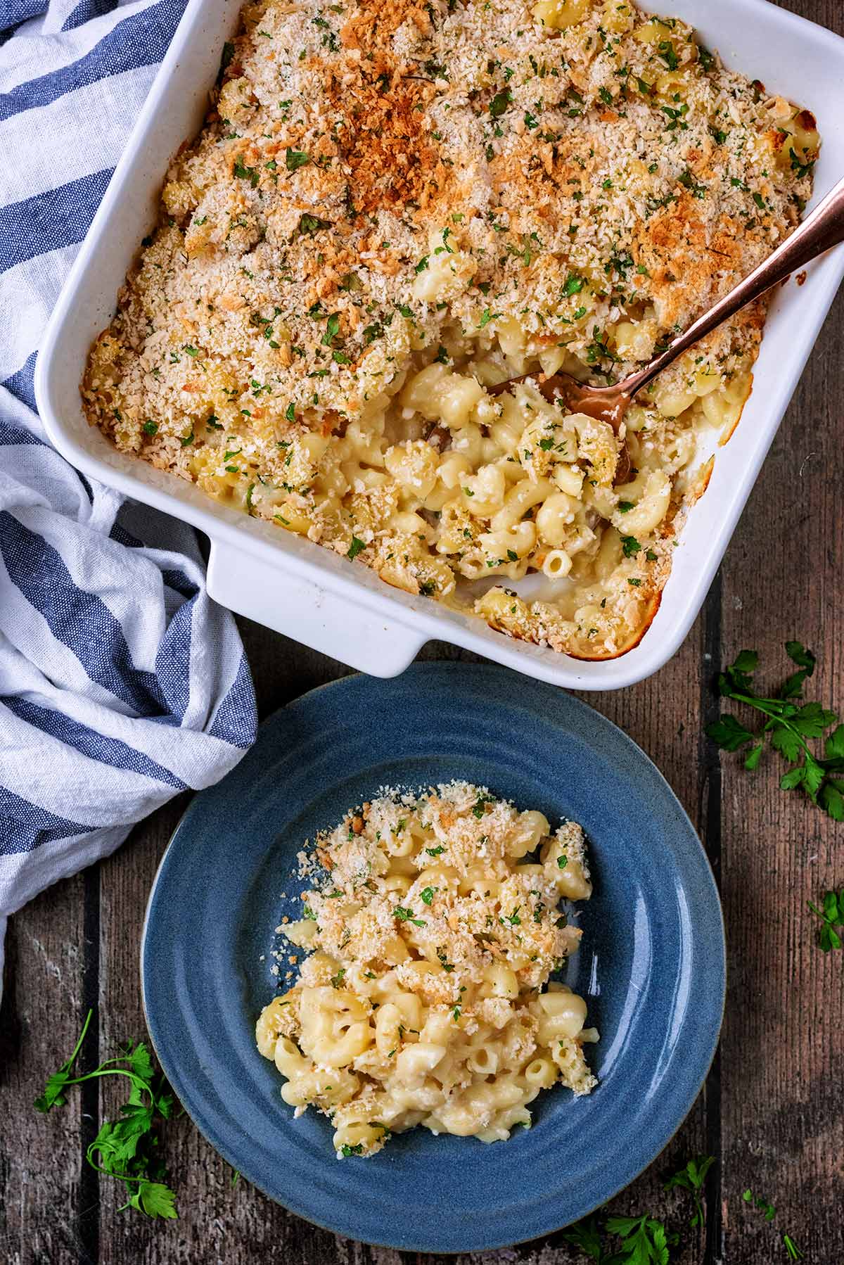 A baking dish full of mac and cheese with a portion removed and put on a plate.