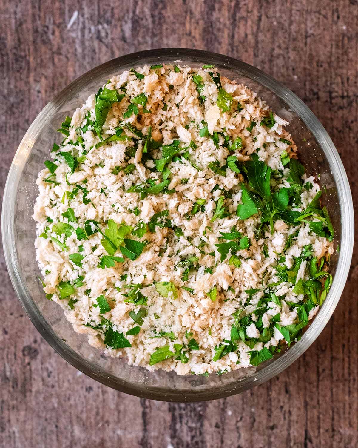 A small glass bowl containing a mixture of breadcrumbs and chopped parsley.