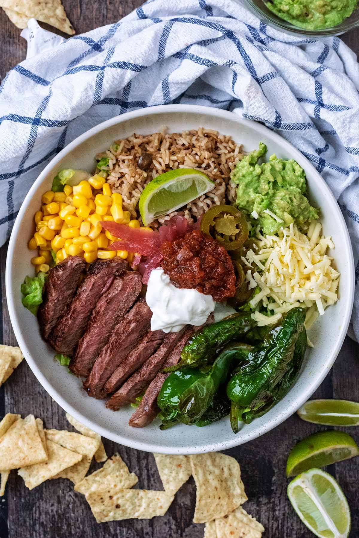 A large bowl wit lettuce, sliced steak, rice, pepeprs, cheese and sauces.