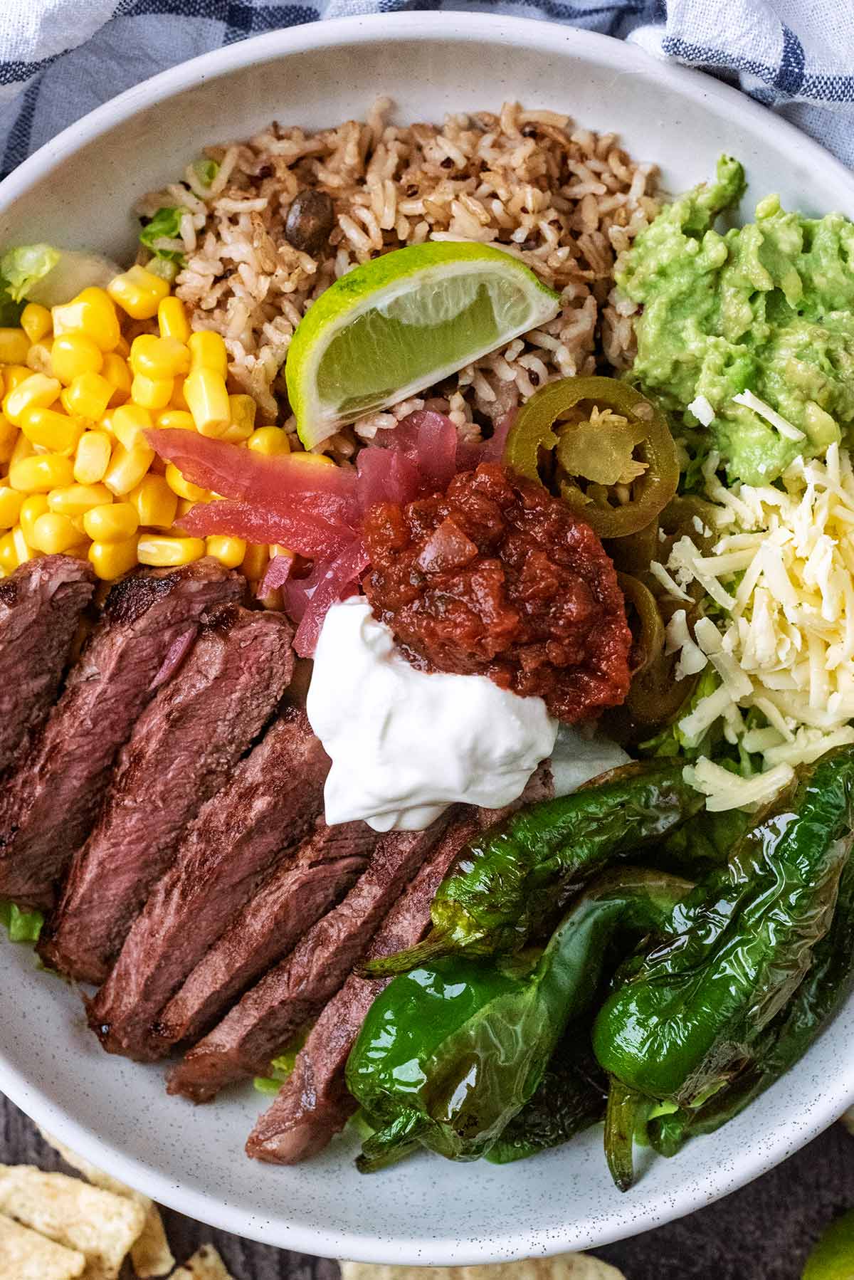 Slices of steak in a bowl with rice and salad items.