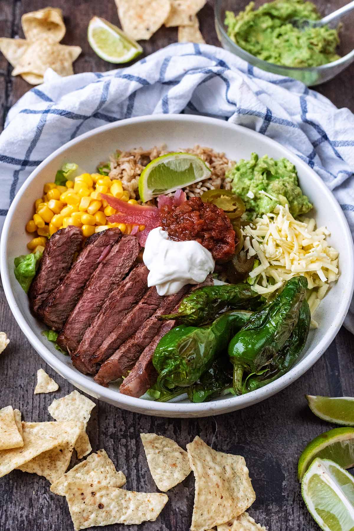 A steak and rice bowl surrounded by tortilla chips and a bowl of guacamole.