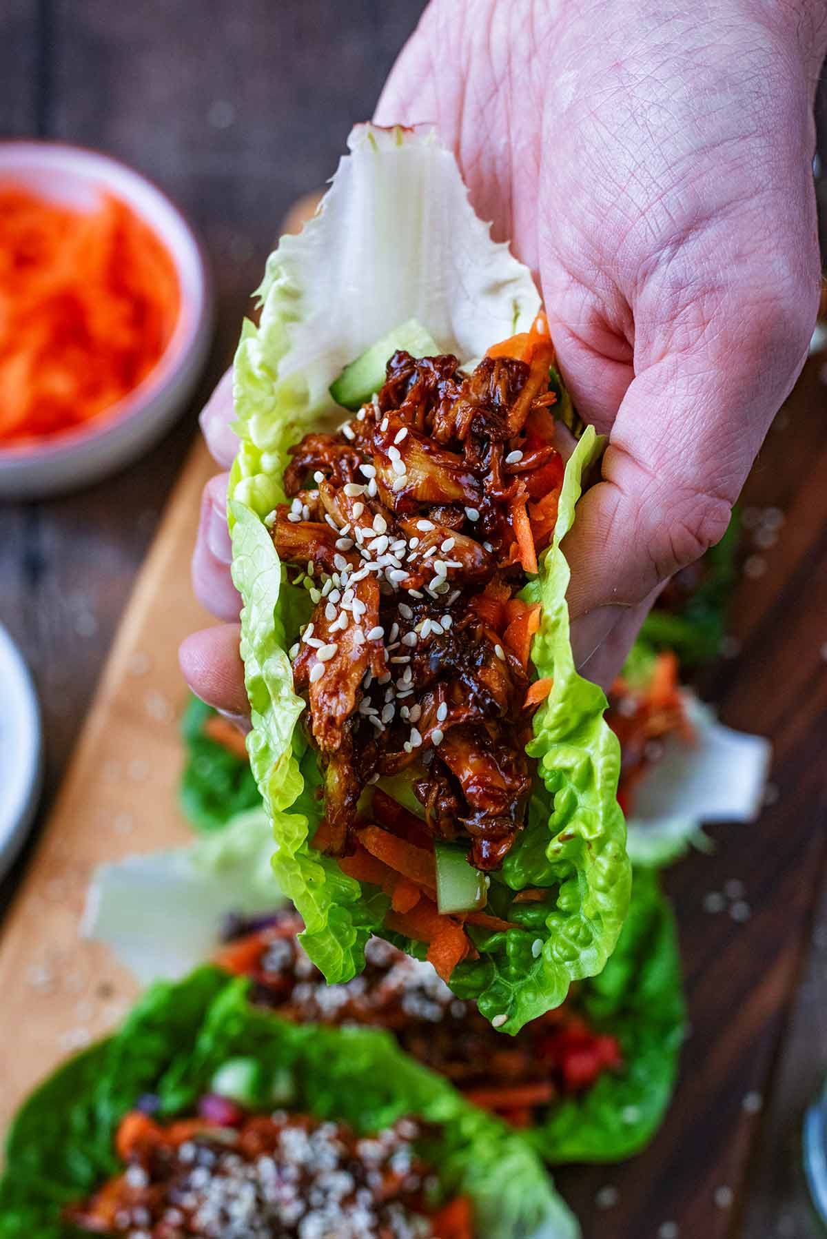 A hand holding a lettuce wrap full of chopped vegetables and teriyaki chicken.