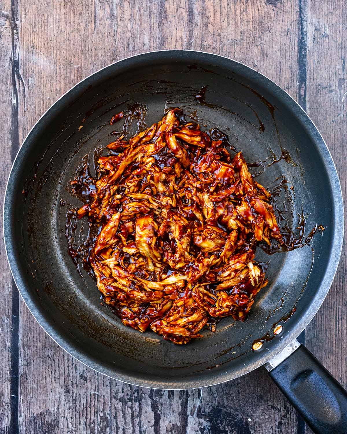 Shredded chicken in teriyaki sauce, cooking in a frying pan.