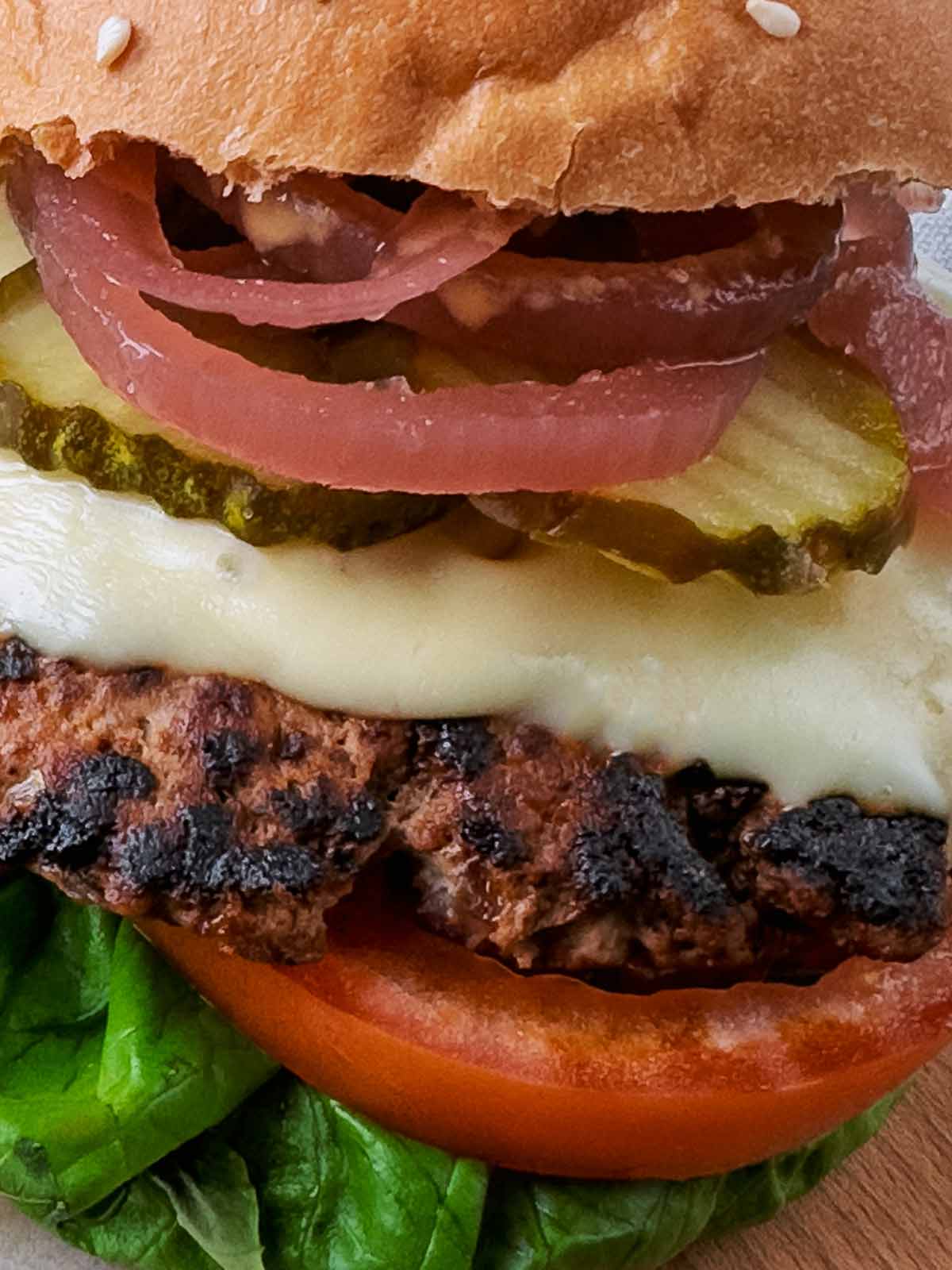 Cooked burger topped with cheese and pickles.