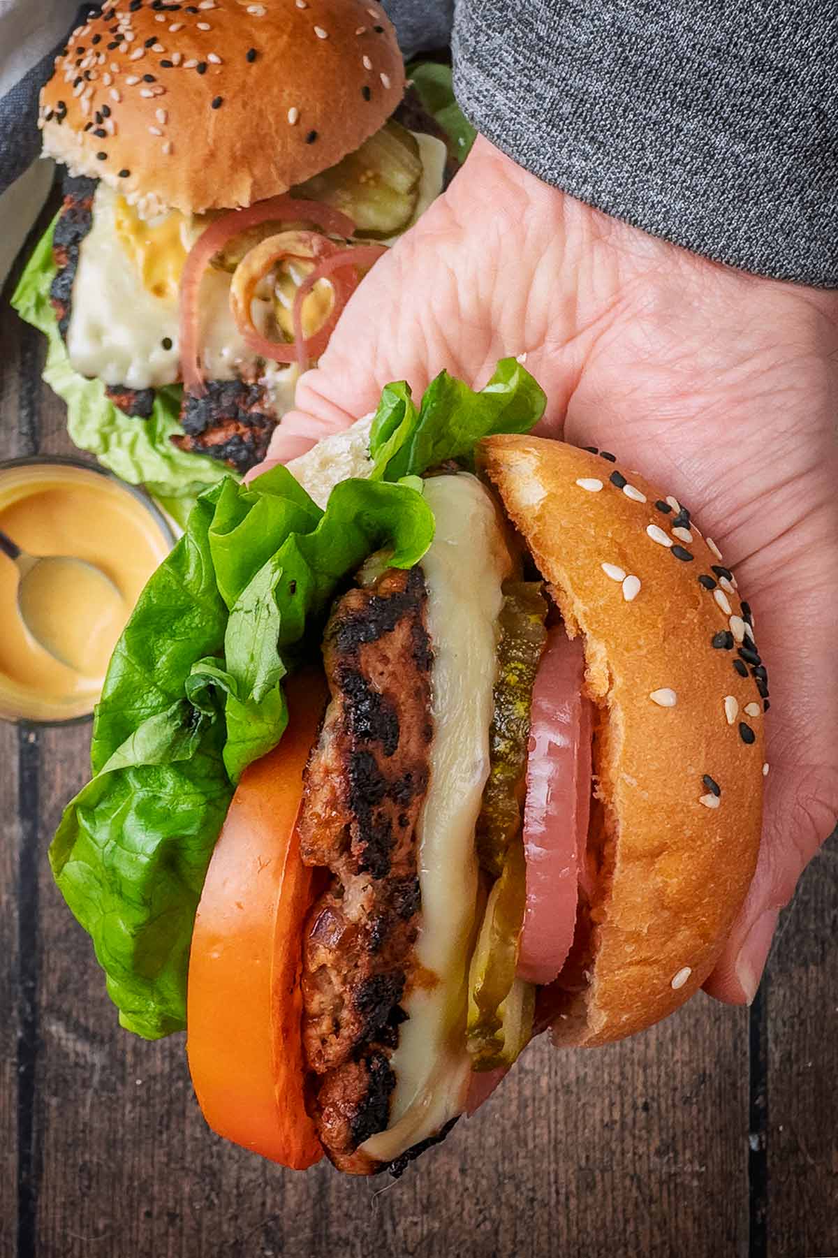 A hand holding a turkey burger in a bun with salad.