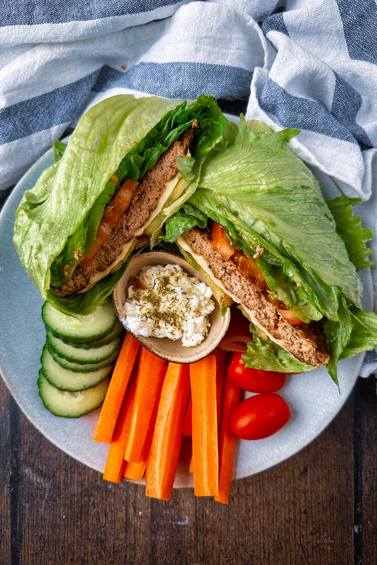 A burger wrapped in a lettuce leaf on a plate with crudites and dip.