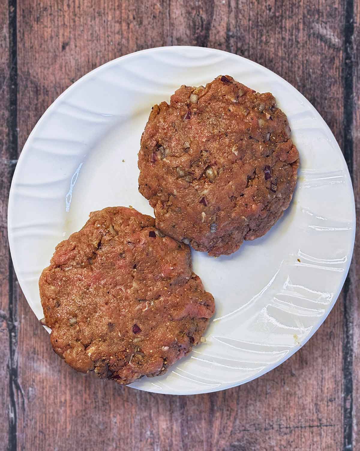 Two burger patties on a white plate.