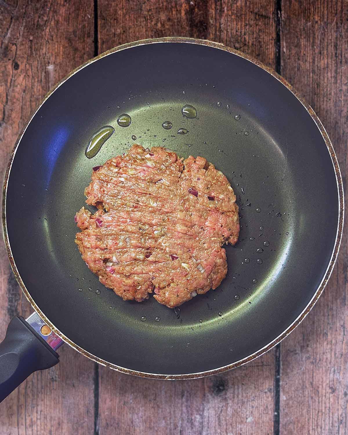 A burger patty frying in a pan.