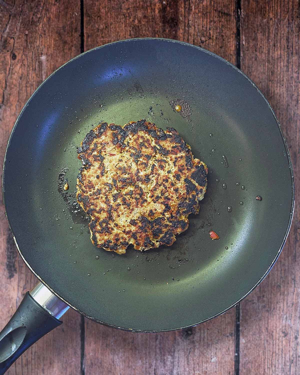 A cooked burger in a frying pan.