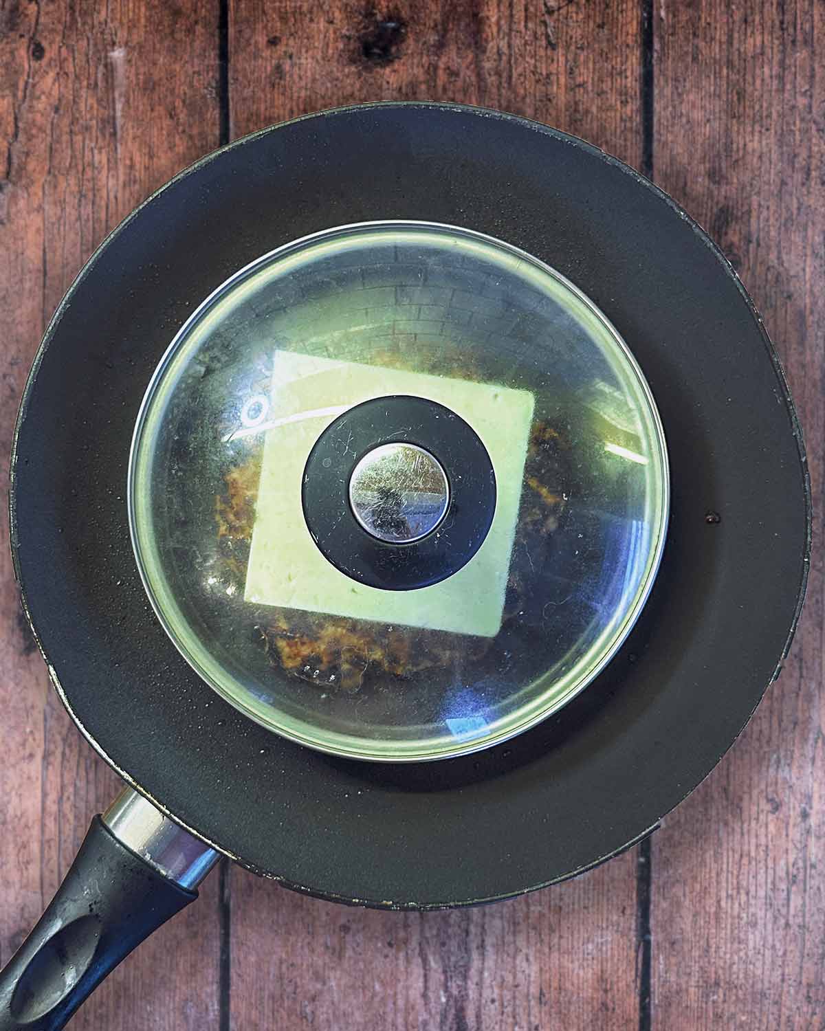 A glass pan lid put over the burger in the pan.