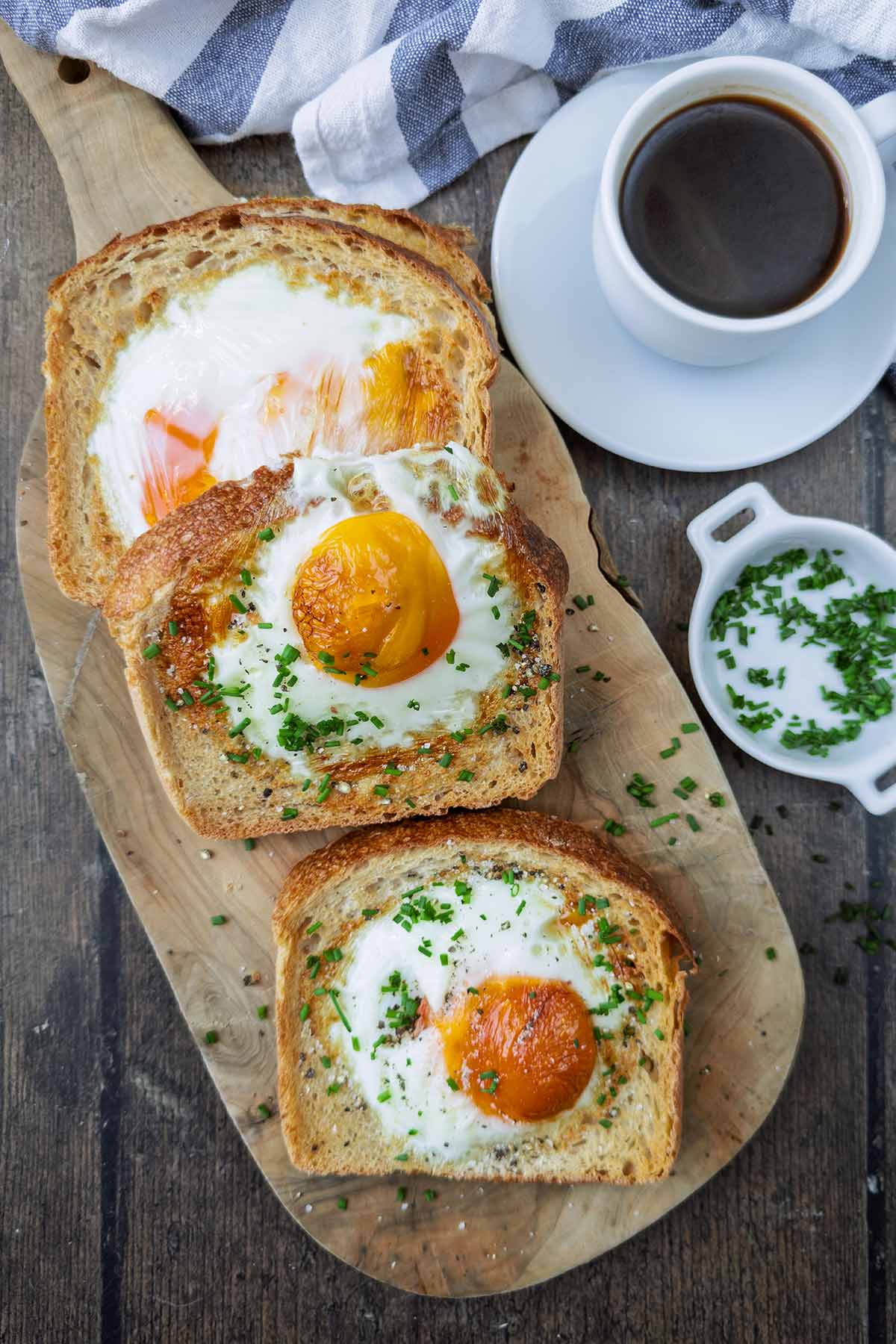 four slices of egg toast on a wooden board, next to a small cup of coffee.