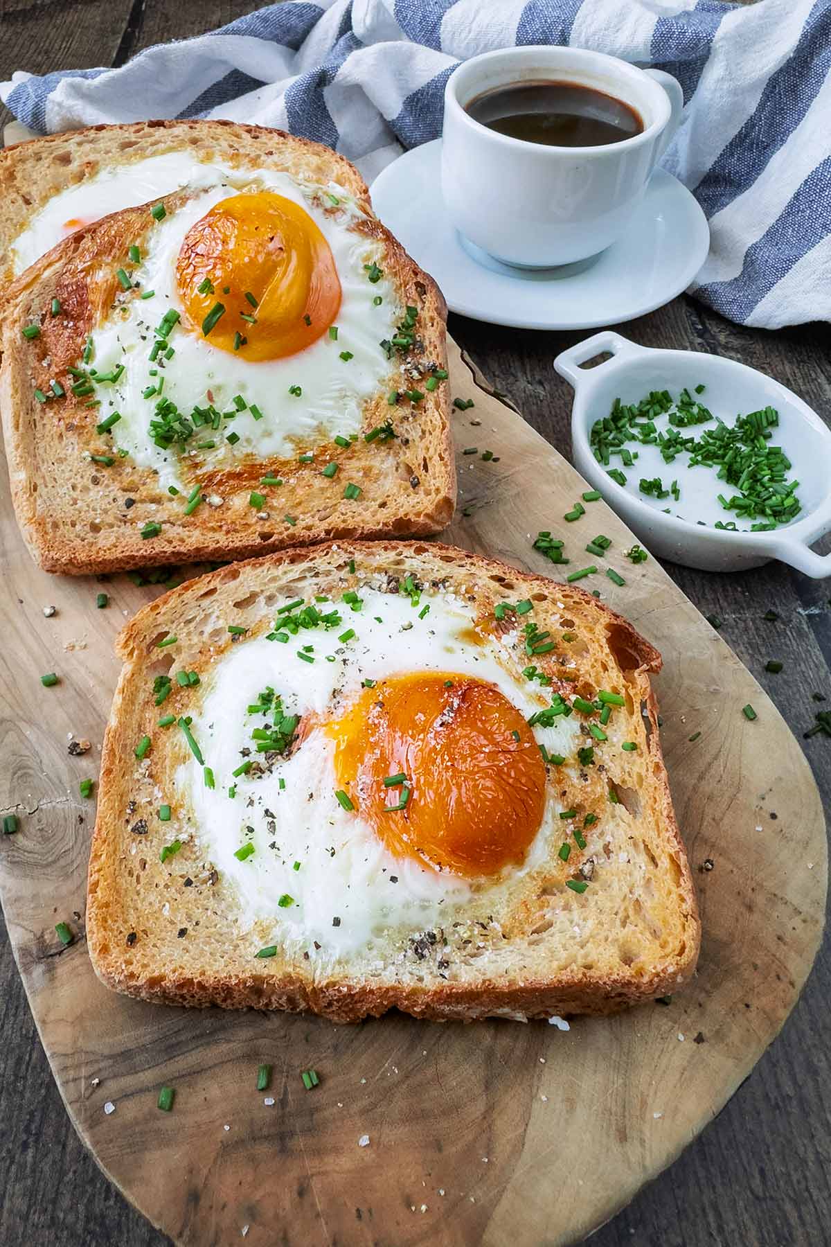 Eggy toast on a wooden board in front of a striped towel and a cup of black coffee.