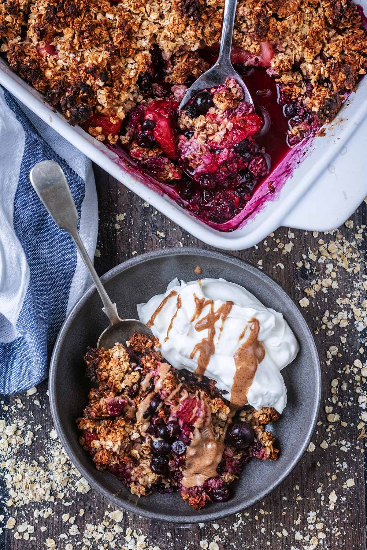 A baking dish full of berry crumble next to a bowl of the crumble with some yogurt.