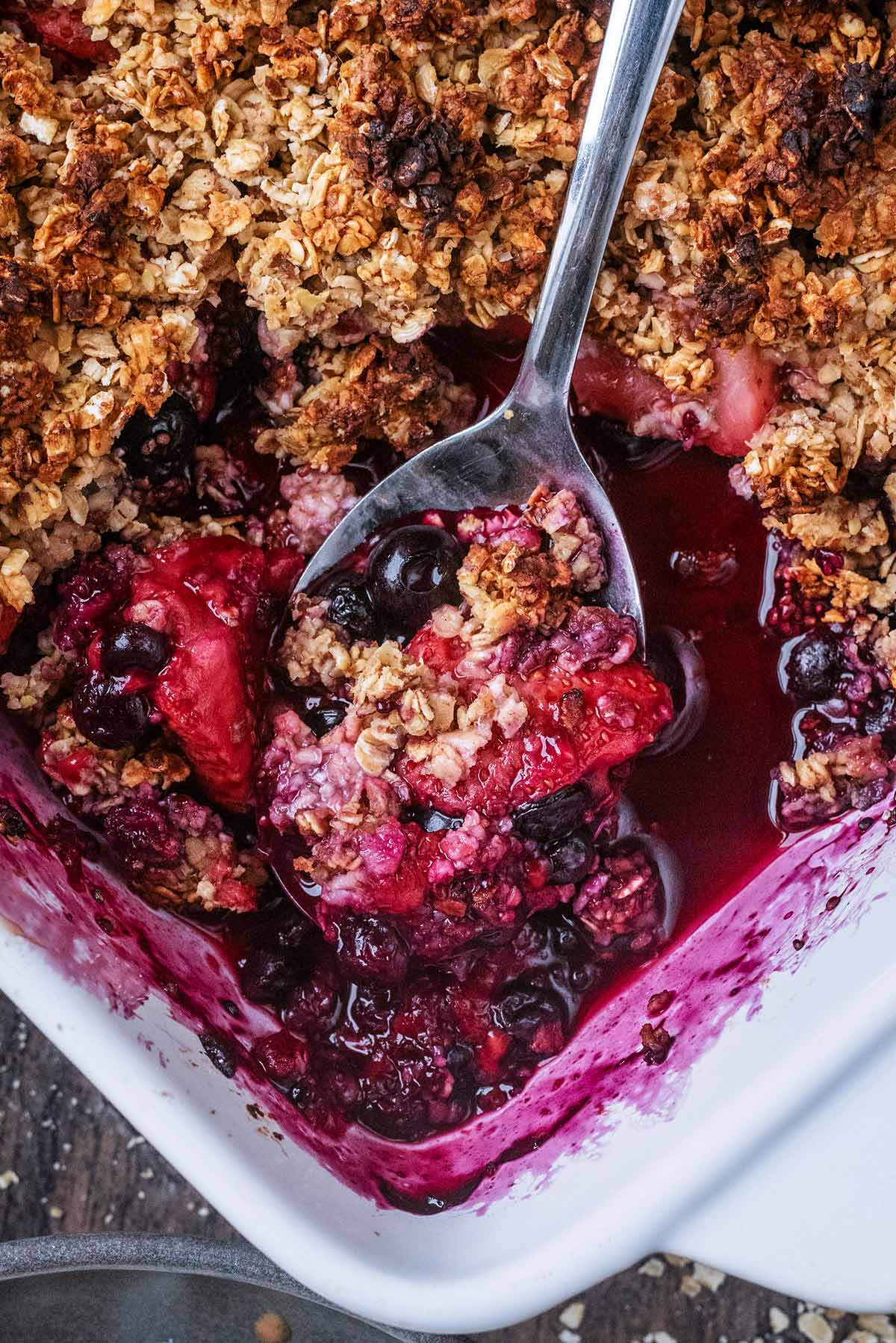 A spoon lifting some berry crumble from a baking dish.