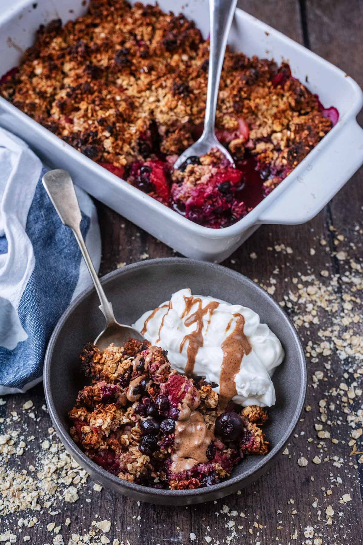 A bowl of crumble and yogurt in front of a baking dish containing more crumble.