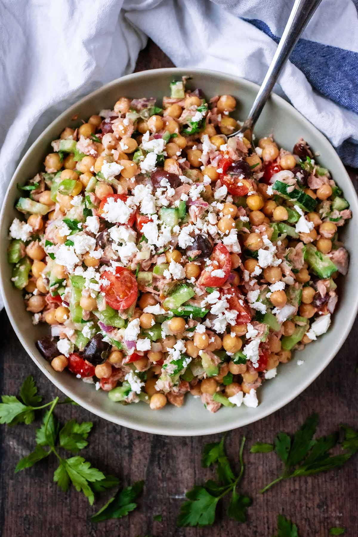 A bowl of chickpea salad next to a white towel and some sprigs of parsley.