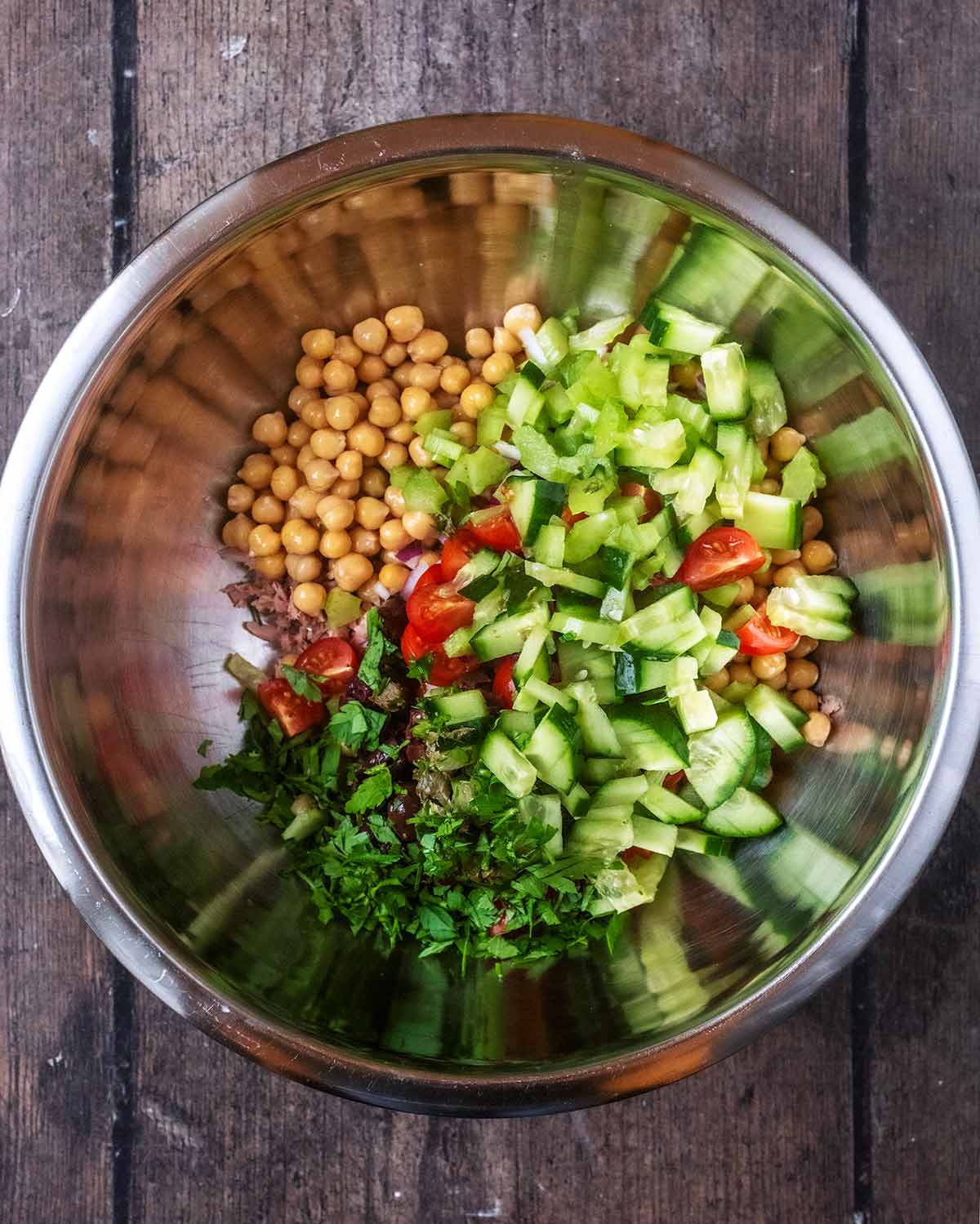 A mixing bowl containing tuna, chickpeas, chopped cucumber, celery, tomatoes and herbs.