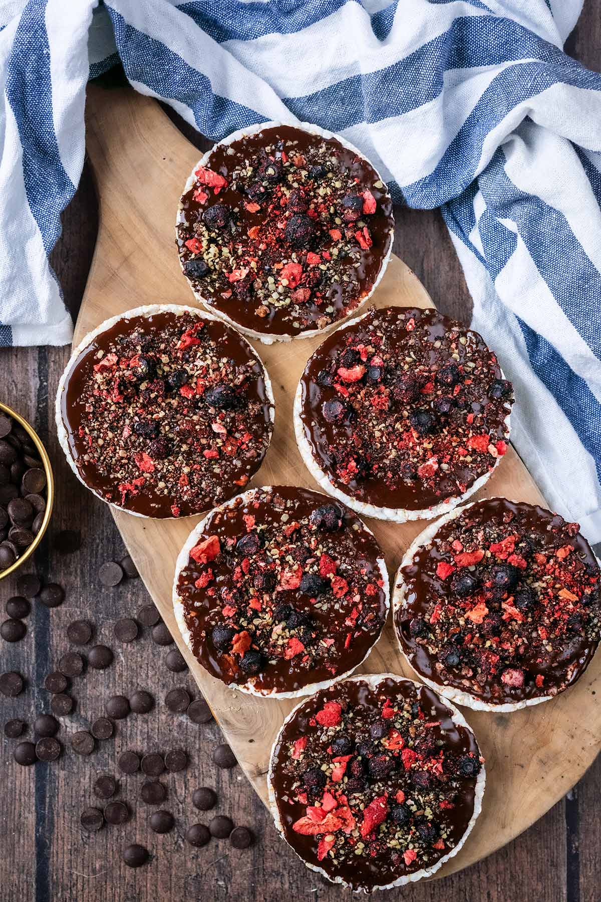 Six chocolate covered rice cakes on a wooden serving board next to a striped towel.