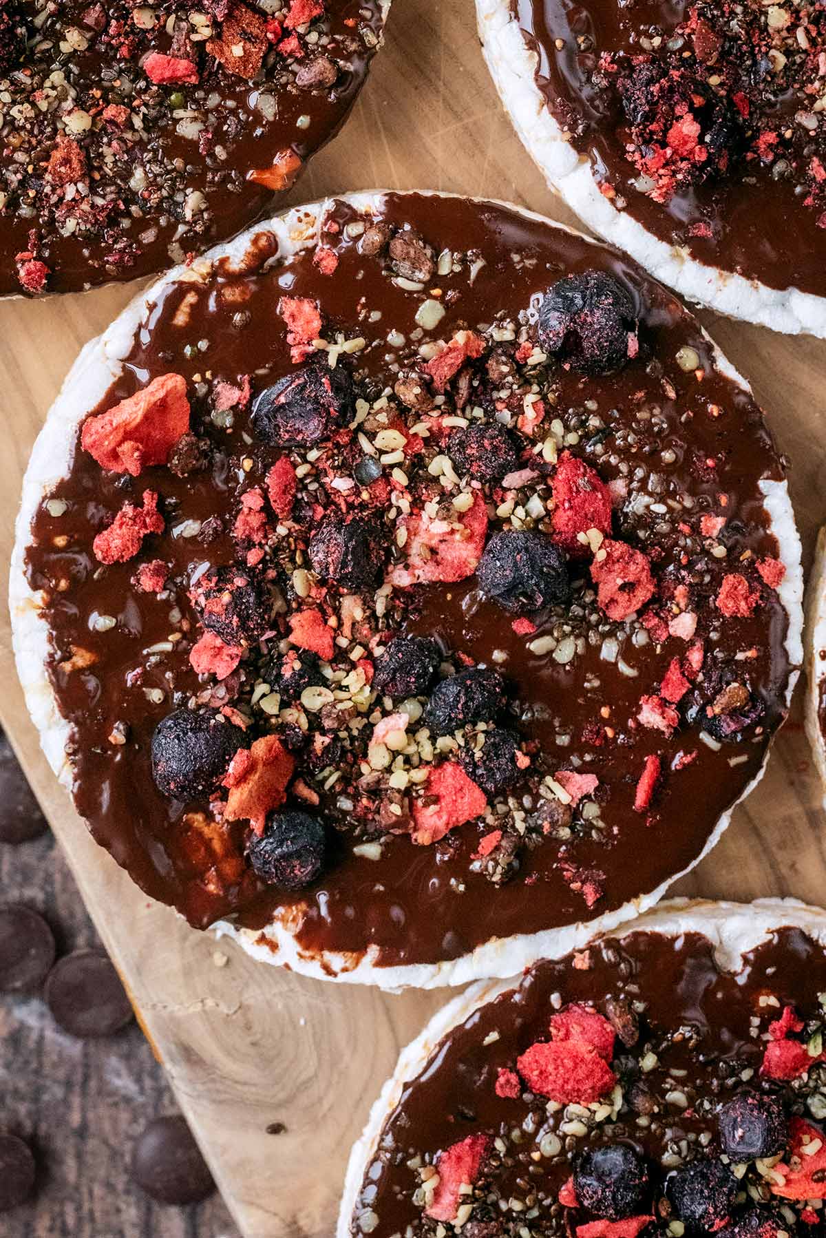 A chocolate covered rice cake topped with crushed nuts and berries.