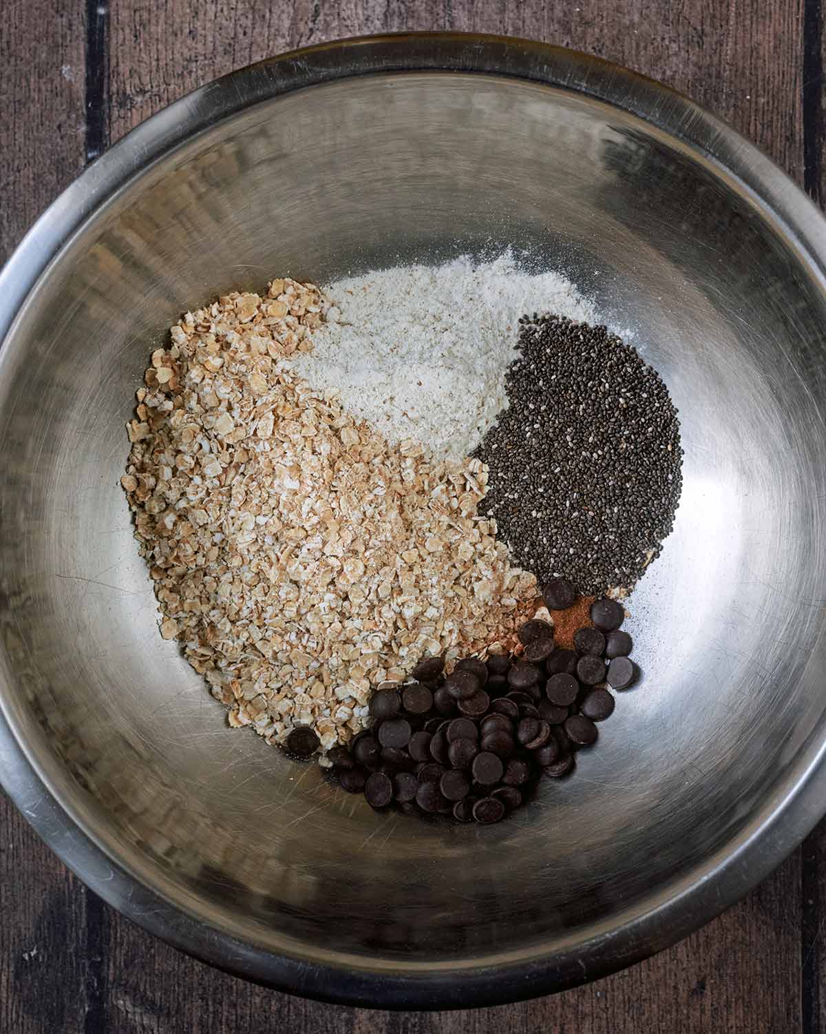 A mixing bowl with oats, protein powder, cinnamon, chia seeds and chocolate chips in it.