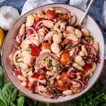 A bowl of Italian bean salad with a spoon in it.