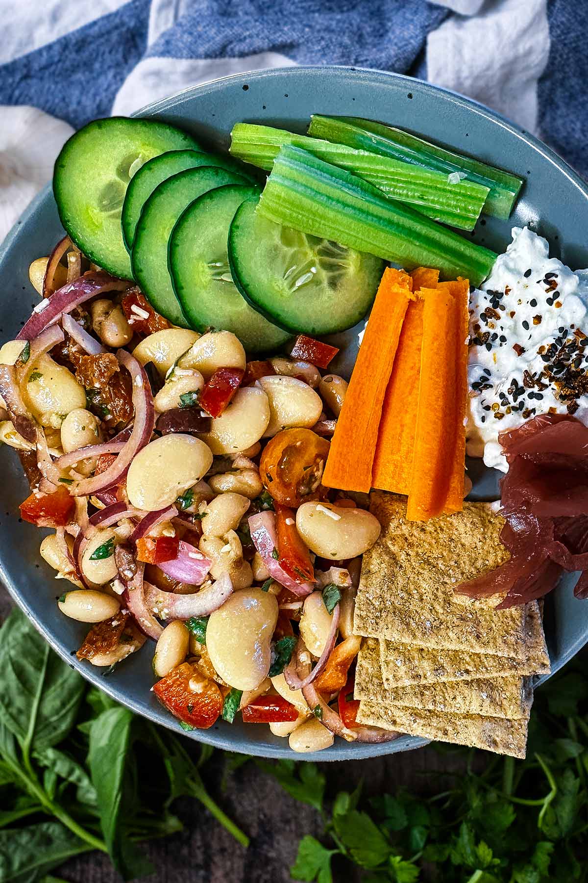 Bean salad on a plate with crudités, cottage cheese dip and some square crackers.